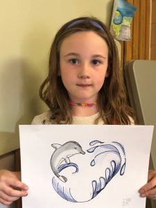 A young girl holding a drawing of a dolphin.